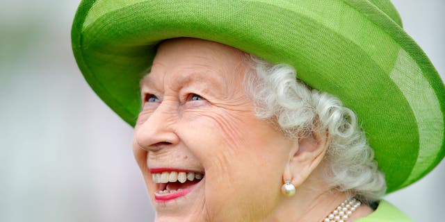 Queen Elizabeth lächelt breit, während sie einen hellgrünen Mantel mit passendem Hut trägt.