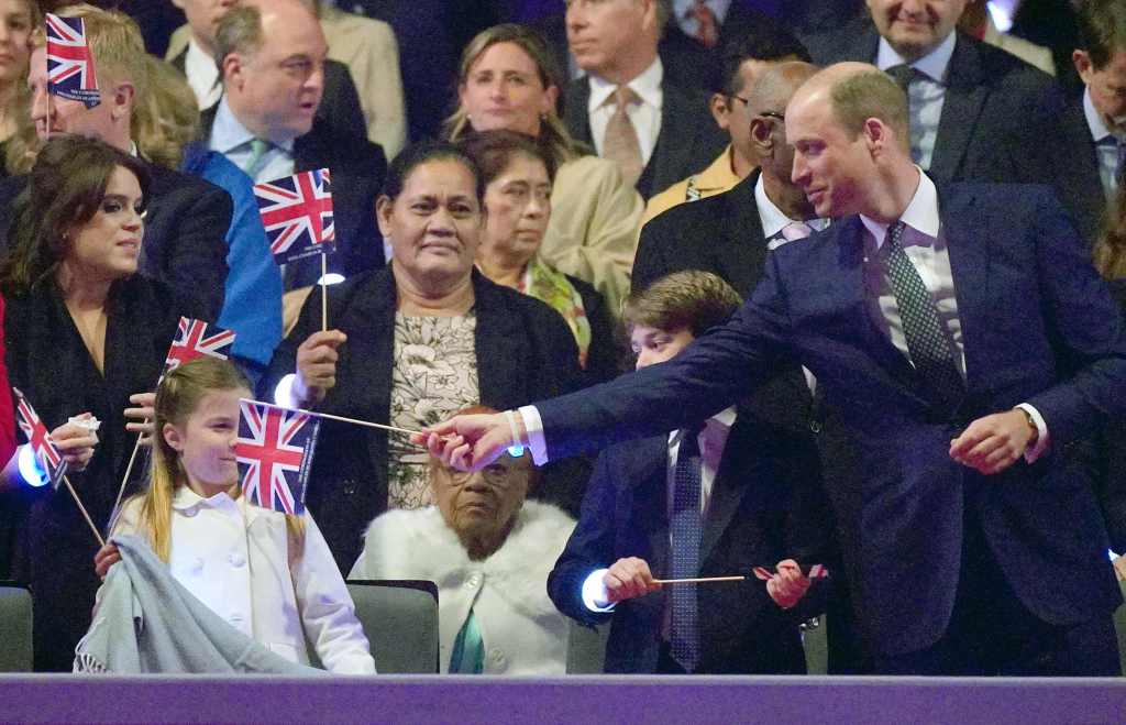 Prinzessin Charlotte von Wales (L) reagiert, beobachtet von ihrem Bruder, dem britischen Prinzen George von Wales (C), während ihr Vater, der britische Prinz William, Prinz von Wales (R), während des Krönungskonzerts mit einer Unionsflagge spielt 