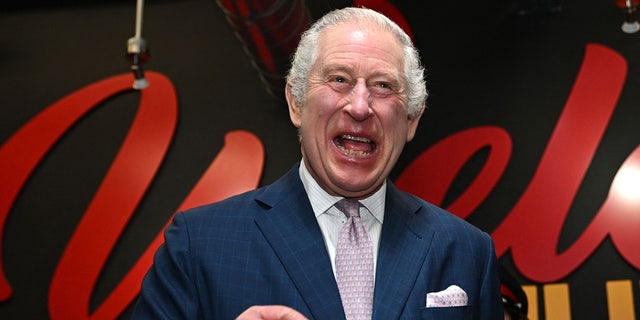 King Charles lacht in einem marineblauen Anzug und einer hellrosa Krawatte, während er in Manchester ist