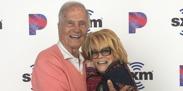 Pat Boone in einem rosa Pullover umarmt eine lächelnde Ann-Margret mit Brille
