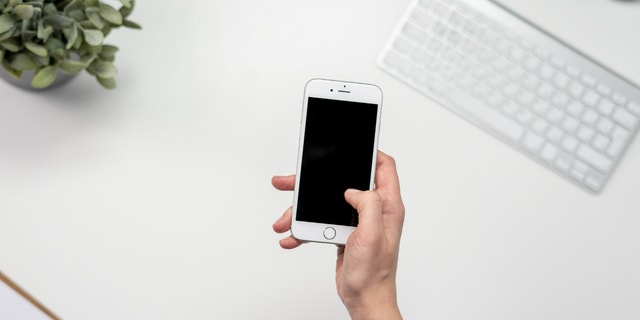 Eine Person hält ihr Telefon über einen weißen Schreibtisch.