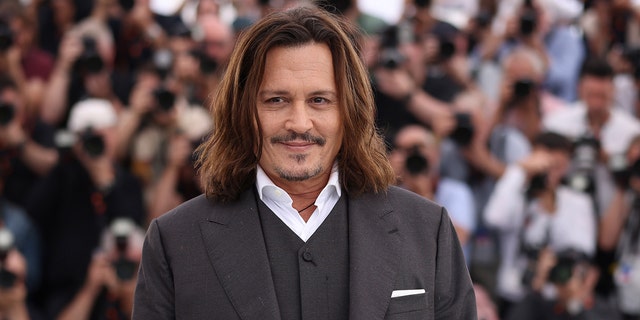 Johnny Depp läuft in einem grauen Anzug und einem weißen Hemd über den roten Teppich der Filmfestspiele von Cannes