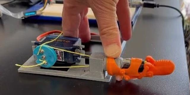 Orangefarbene 3D-gedruckte kleine Fingerprothese auf einem Gerät mit der Hand eines Mannes darauf