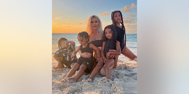 Kim Kardashian sitzt mit ihren vier Kindern am Strand und balanciert lachend Chicago und Psalm, neben ihr North und Saint
