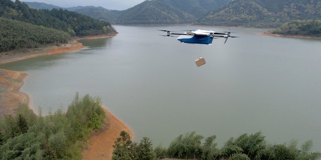 Foto einer Drohne, die eine Kiste über einen See trägt.