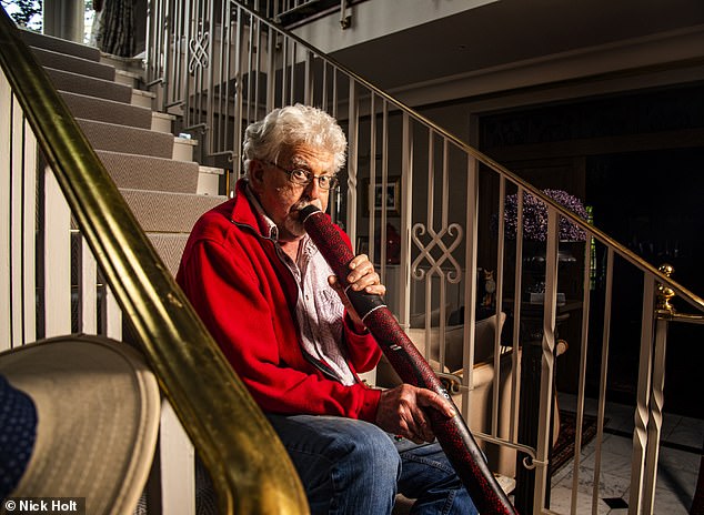 Harris posiert mit seinem Digeridoo auf einer großen Treppe, bevor er in das Instrument bläst und dabei in die Linse schaut
