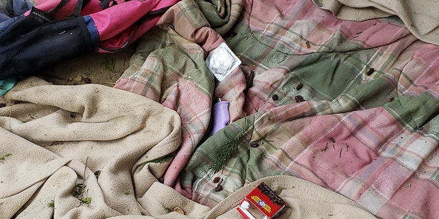 Unbenutzte Kondompackung neben lila Feuerzeug auf rosa und grüner Flanelldecke