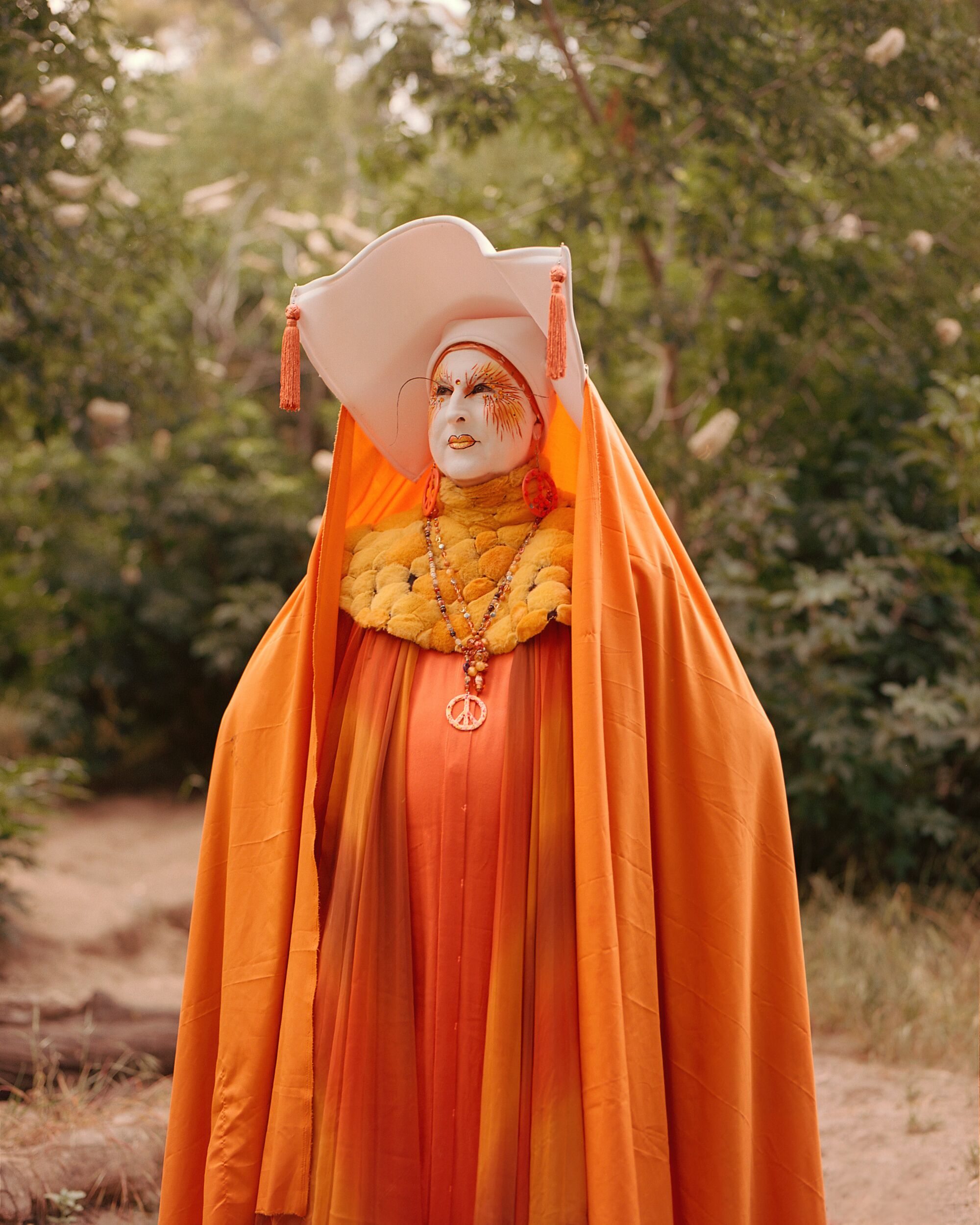 Eine Drag-Nonne mit weißer Gesichtsbemalung, Wimpole und aufwendigem orangefarbenem Kleid und Umhang.