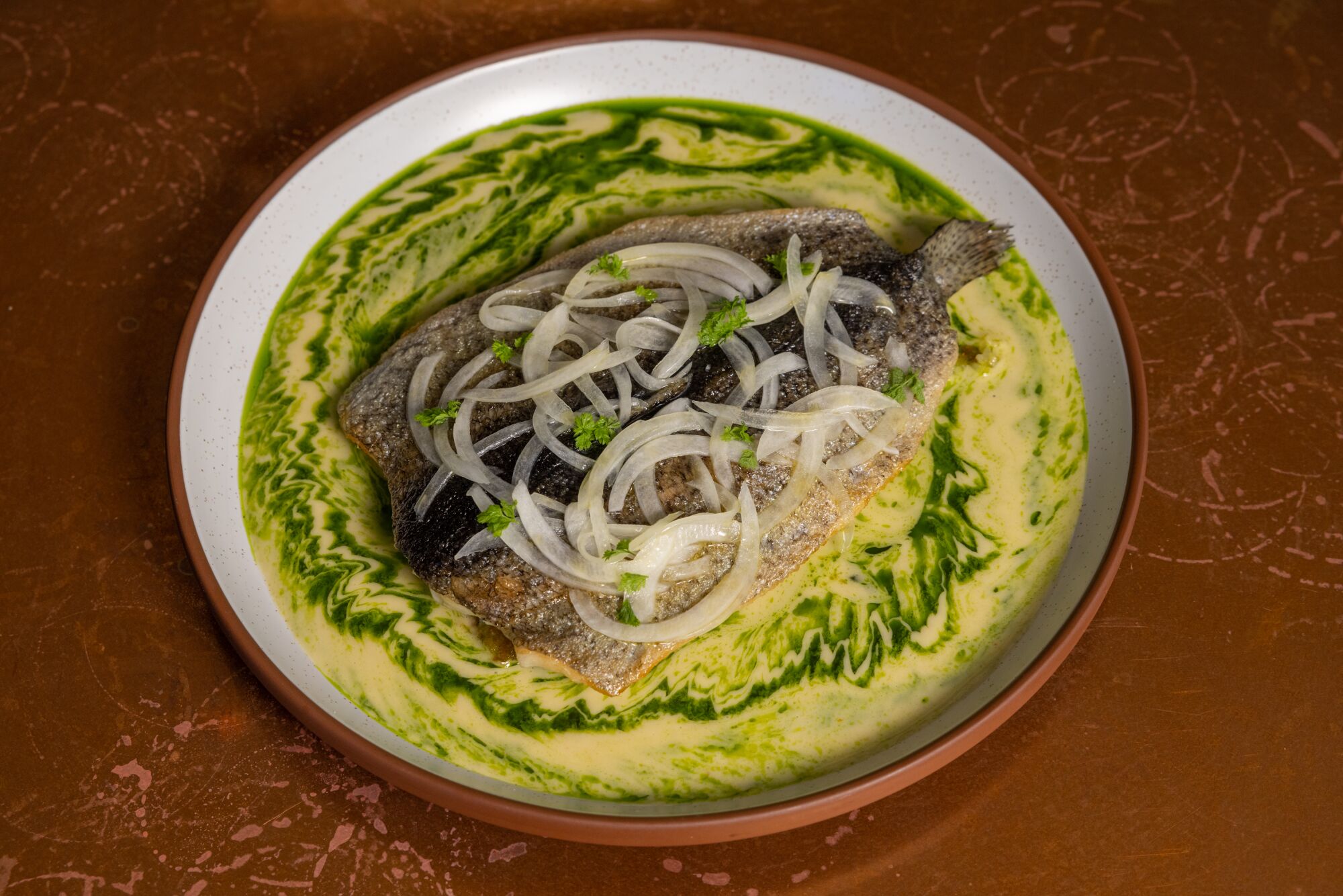 Ein Teller mit Forellen, garniert mit Zwiebeln und in einer gelb-grünen Soße