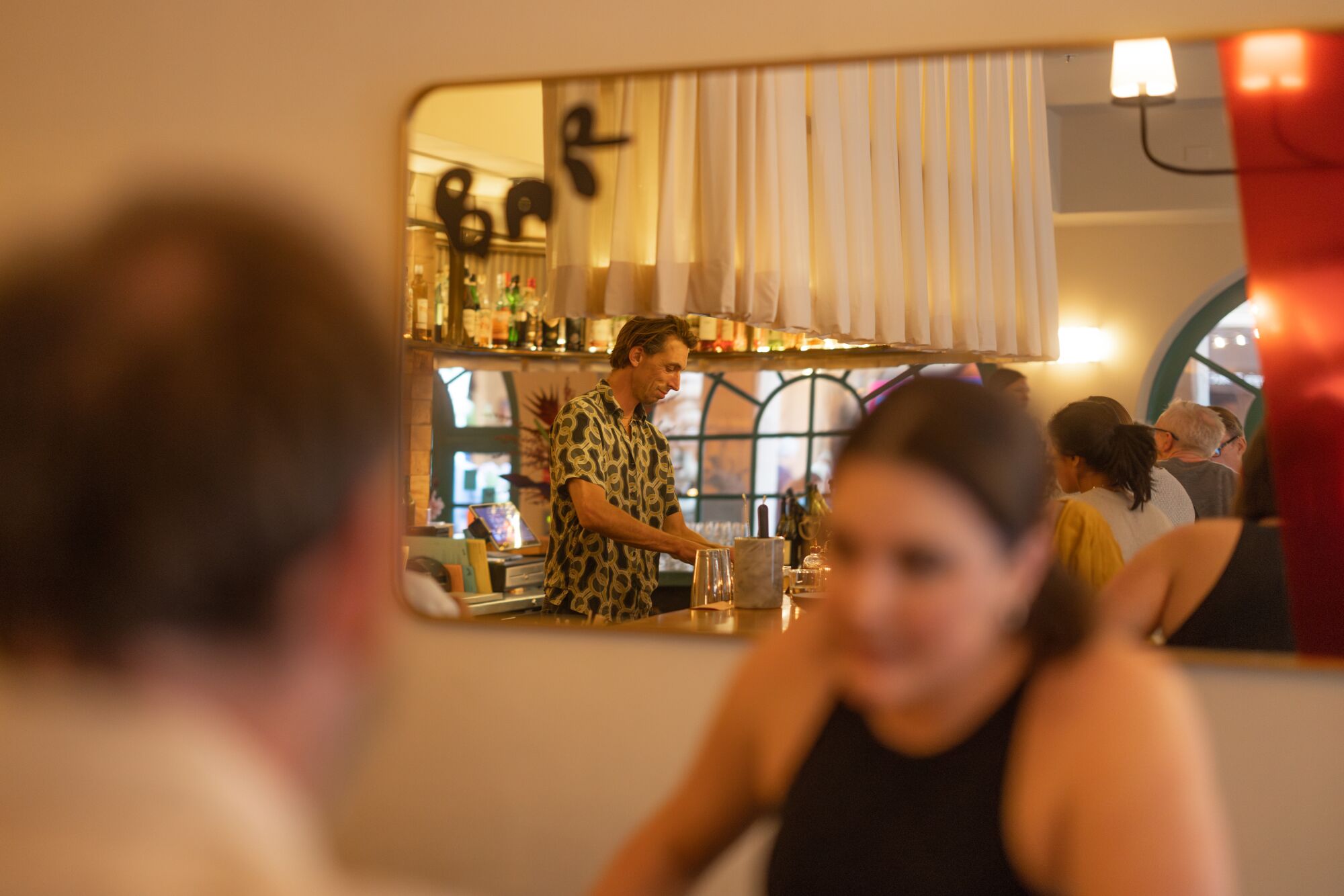 Ein Paar speist in der Bar Chelou, während ein Barkeeper im Spiegelbild Getränke zubereitet.