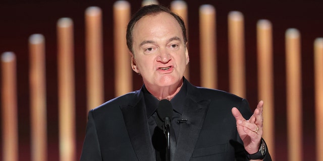 Quentin Tarantino spricht bei den Golden Globes in ein Mikrofon und trägt einen komplett schwarzen Anzug
