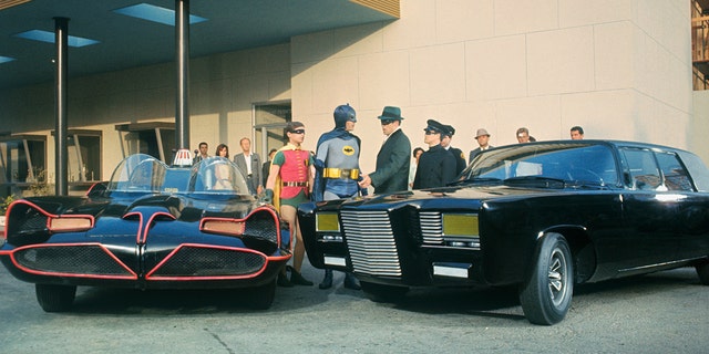 Die Besetzung von The Green Hornet und Batman in Kostümen neben Autos