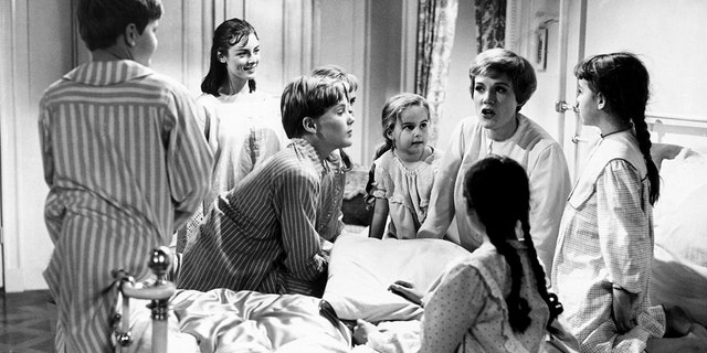 Julie Andrews in bed wearing pajamas telling the von trapp children a story