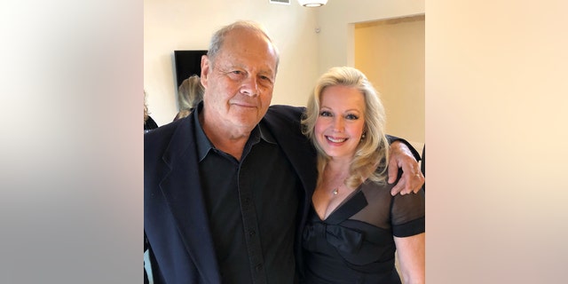 Kym Karath wearing a black dress with her filmmaker who has his arms around her