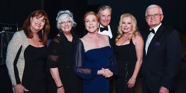 The cast of the sound of music wearing various shades of black and navy posing together for a photo