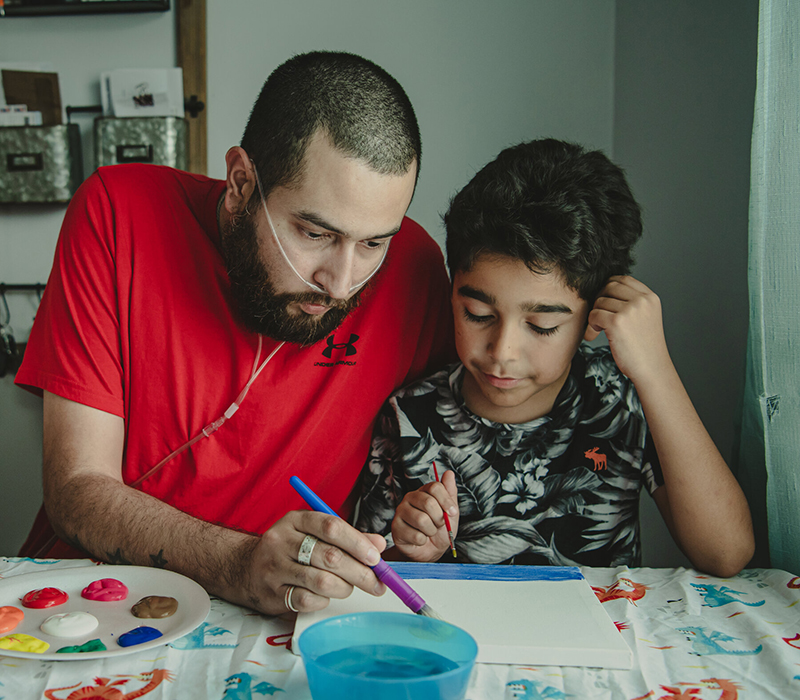 Andy Muñoz sits at a table and helps his two young sons paint and color.