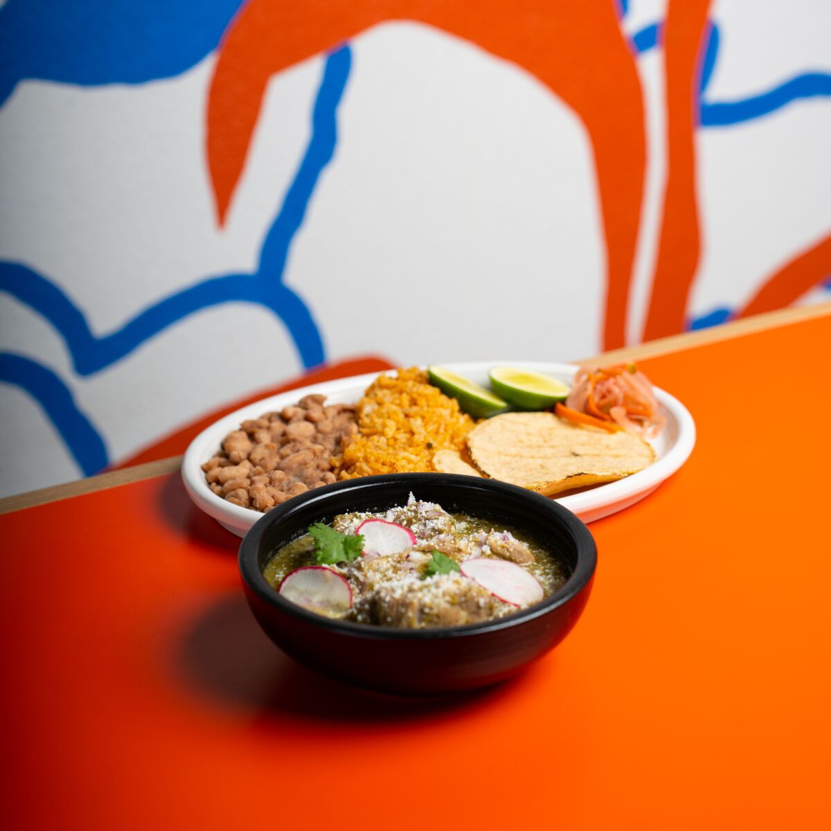 Eine Schüssel mit scharfem Fleisch mit einem Teller Reis und Bohnen auf einem orangefarbenen Tisch bei David Kuo's Fatty Mart in Mar Vista.