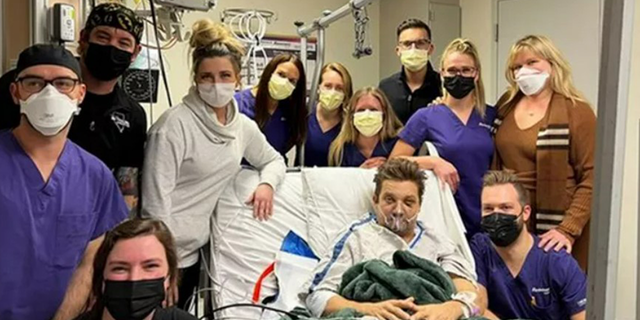 Jeremy Renner liegt mit grüner Decke und Sauerstoffmaske in einem Krankenhausbett, umgeben von medizinischem Personal im Krankenhaus