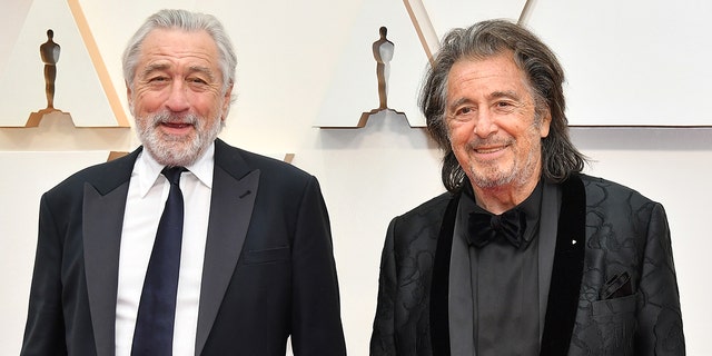 Robert De Niro lächelt in schwarzem Anzug und Krawatte neben Al Pacino im schwarzen Anzug bei der Oscar-Verleihung 2020