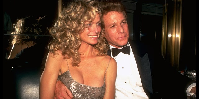 Farrah Fawcett in a sparkly dress cuddling up next to Ryan ONeal in a suit and bowtie