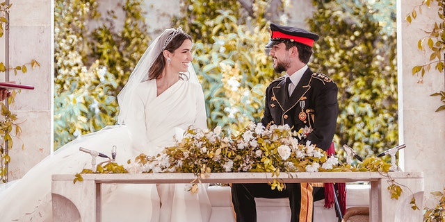 The royal bride and groom sitting together in front of a table with flowers