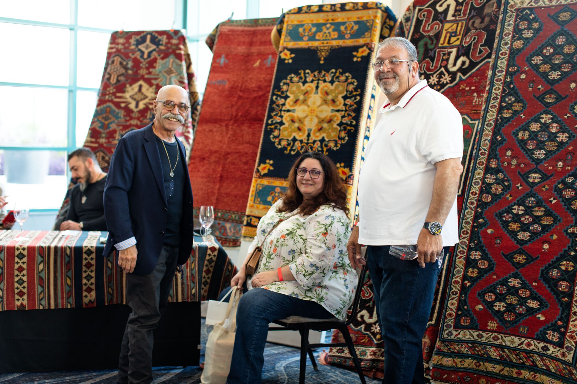 Zwei Männer und eine Frau vor einer Ausstellung handgefertigter Teppiche.