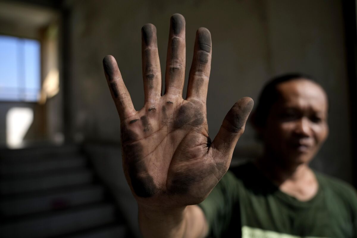 Cecep Supriyadi zeigt seine schmutzige Hand, nachdem er ein Netz berührt hat, das installiert wurde, um Staubpartikel zu verhindern.