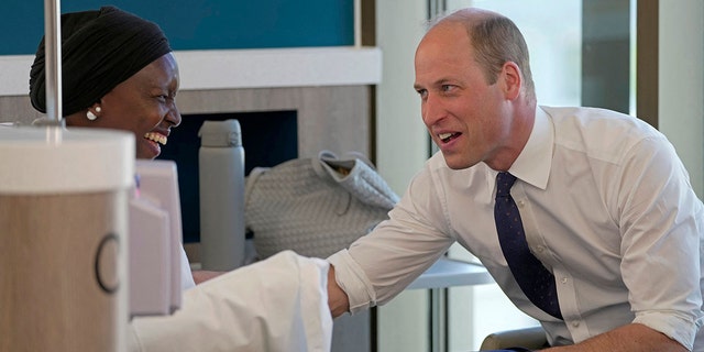 Prinz William trägt ein hochgekrempeltes weißes Hemd und eine Krawatte und spricht mit einer Frau in weißem Outfit