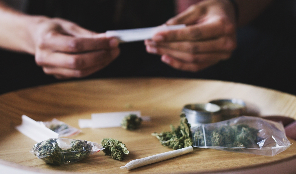 Marihuana auf dem Tisch, während Mann einen Joint dreht. 