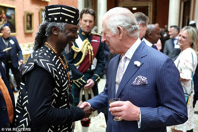 König Charles schüttelt einem Gast während eines Empfangs anlässlich des 75. Jahrestages der Ankunft von HMT Empire Windrush im Buckingham Palace die Hand
