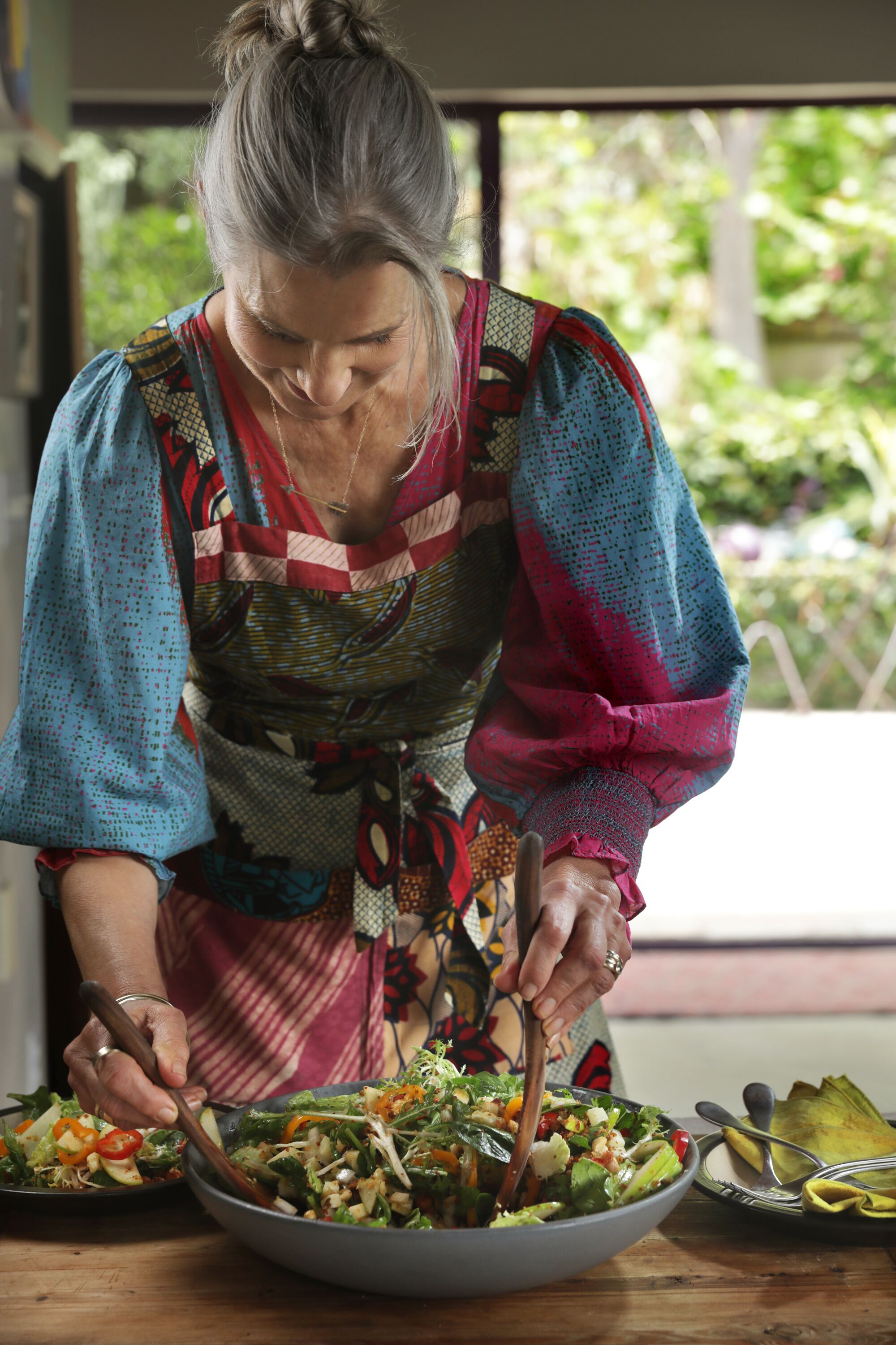 Eine Frau in einer Küche beugt sich über eine Schüssel Salat auf einer Arbeitsplatte.