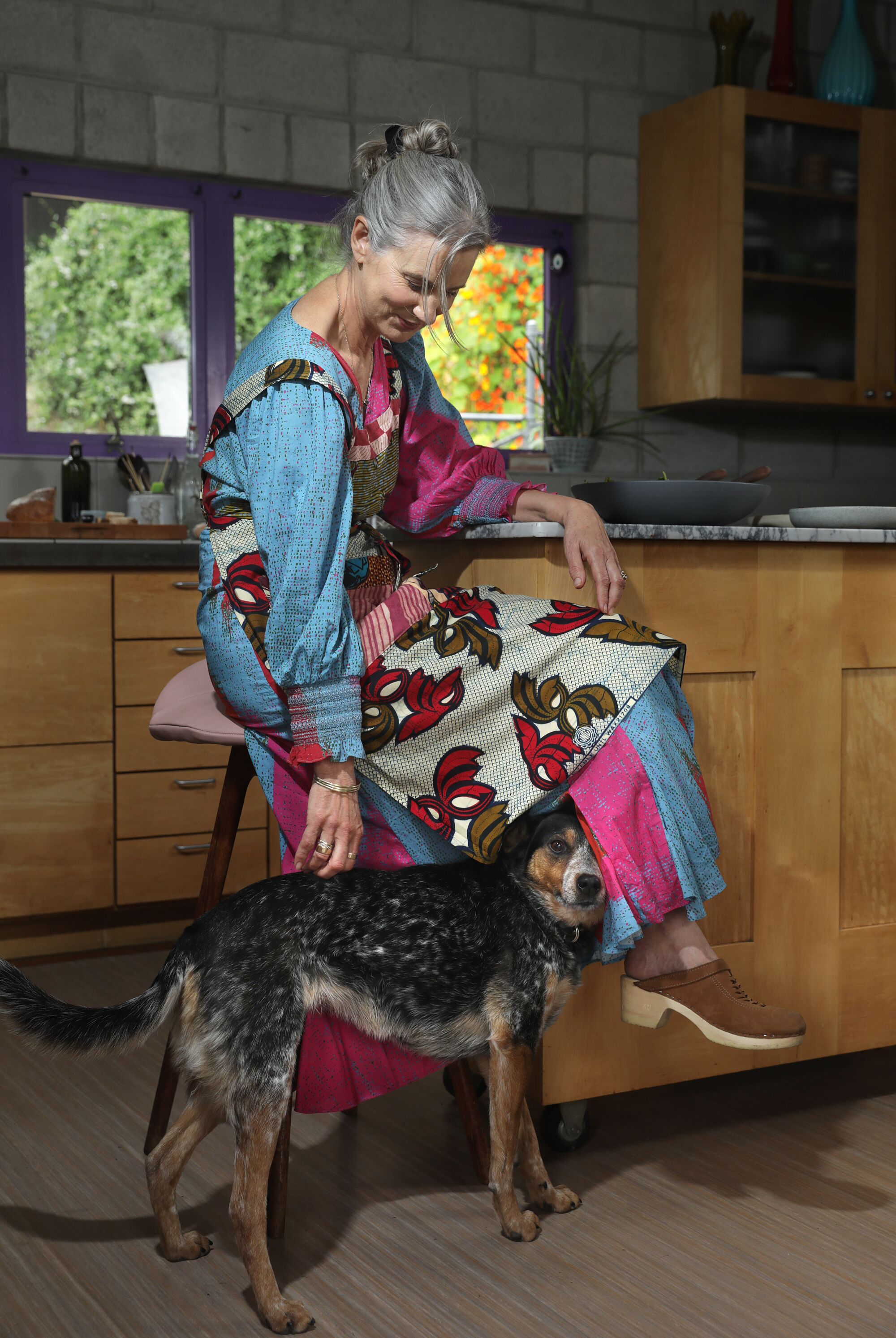 Eine Frau, die an einer Küchentheke sitzt, bückt sich, um ihren Hund zu streicheln.