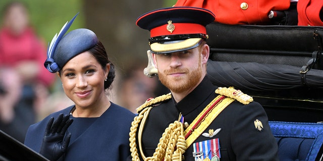 Meghan Markle in einem blauen Kleid und passendem Hut sitzt neben Prinz Harry in seiner Militäruniform
