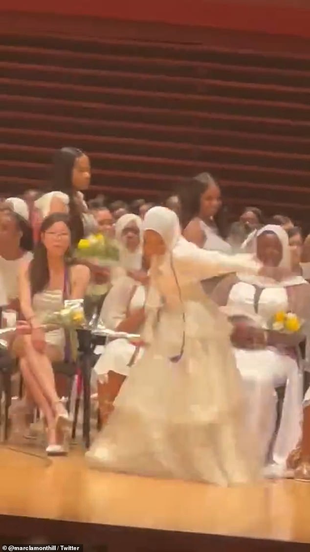 Abdur-Rahman, ganz in Weiß gekleidet und mit gelben Blumen ausgestattet, tanzt, während sie sich der Rektorin nähert, die ihr Diplom in der Hand hält