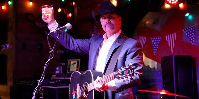John Rich hält in der Bar in Nashville ein Whiskeyglas in die Luft und eine Gitarre um den Hals