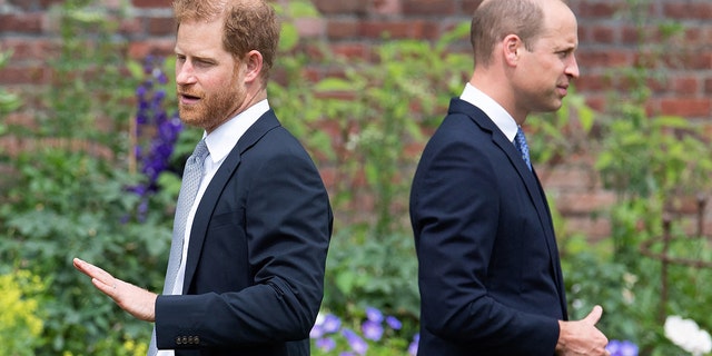 Prinz William und Prinz Harry stehen sich mit dem Rücken zugewandt in passenden Marineanzügen gegenüber