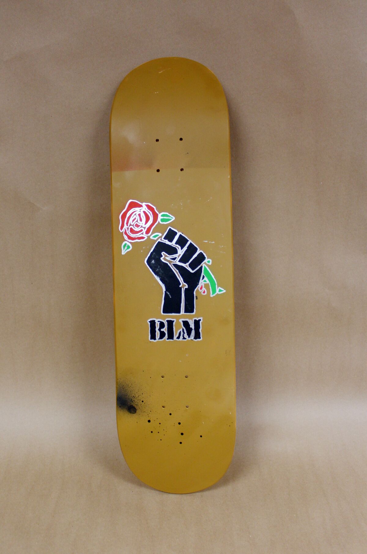 Ein Skateboard mit geballter, erhobener Faust, das eine rote Rose über den Buchstaben BLM hält.