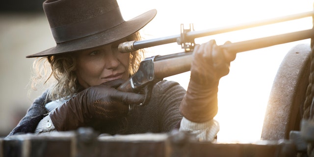 Faith Hill schießt mit einer Waffe, während sie einen Cowboyhut trägt.