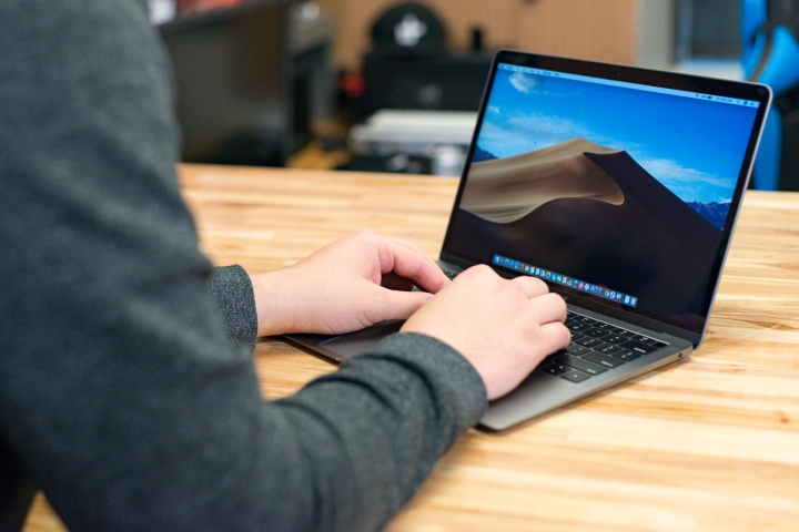 Die Hände einer Person ruhen auf einem 2018 MacBook Air, das auf einem Holztisch liegt.