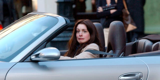 Ein Foto von Anne Hathaway, die am Steuer eines Autos eine Grimasse zieht.