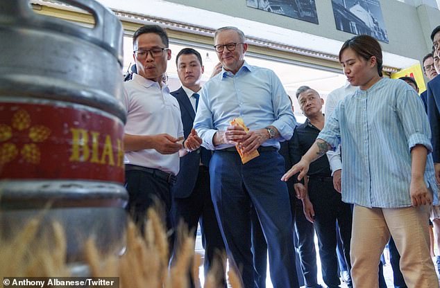 Auf dem Bild (Mitte) hält Premierminister Anthony Albanese ein Banh-Mi-Sandwich und blickt auf ein Bierfass