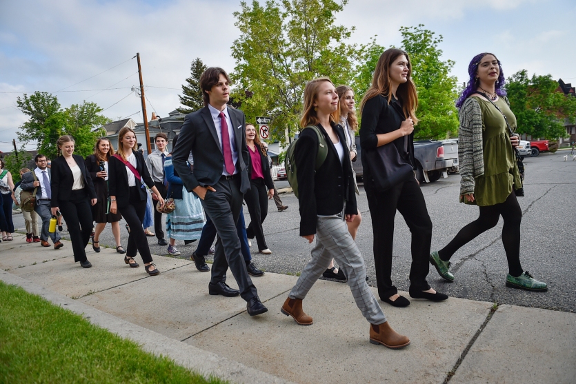 Eine Gruppe Jugendlicher unterschiedlichen Alters in Geschäftskleidung geht einen Bürgersteig entlang.