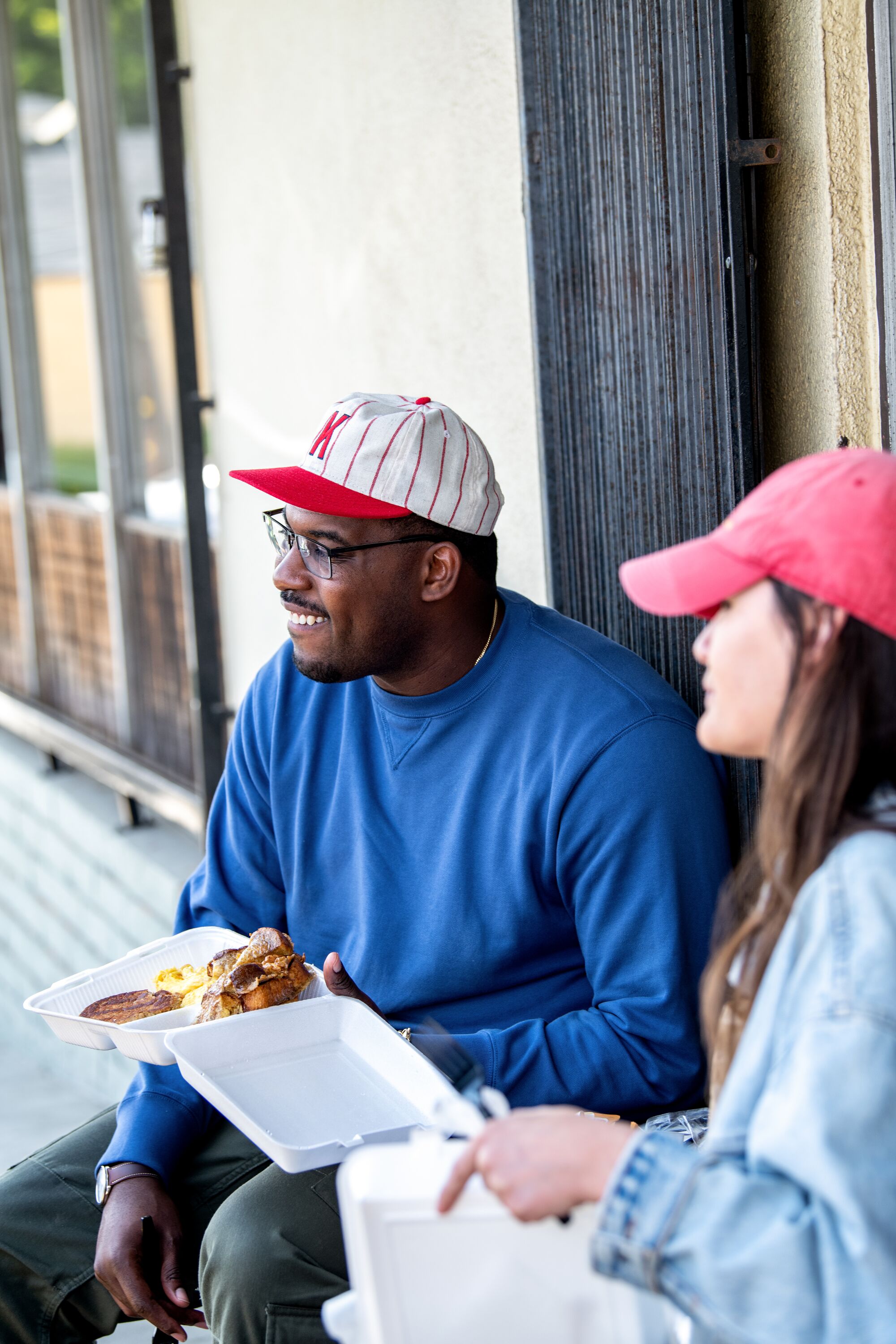 Lionel Boyce und die Food-Kolumnistin der Los Angeles Times, Jenn Harris, sitzen draußen mit Essen zum Mitnehmen.