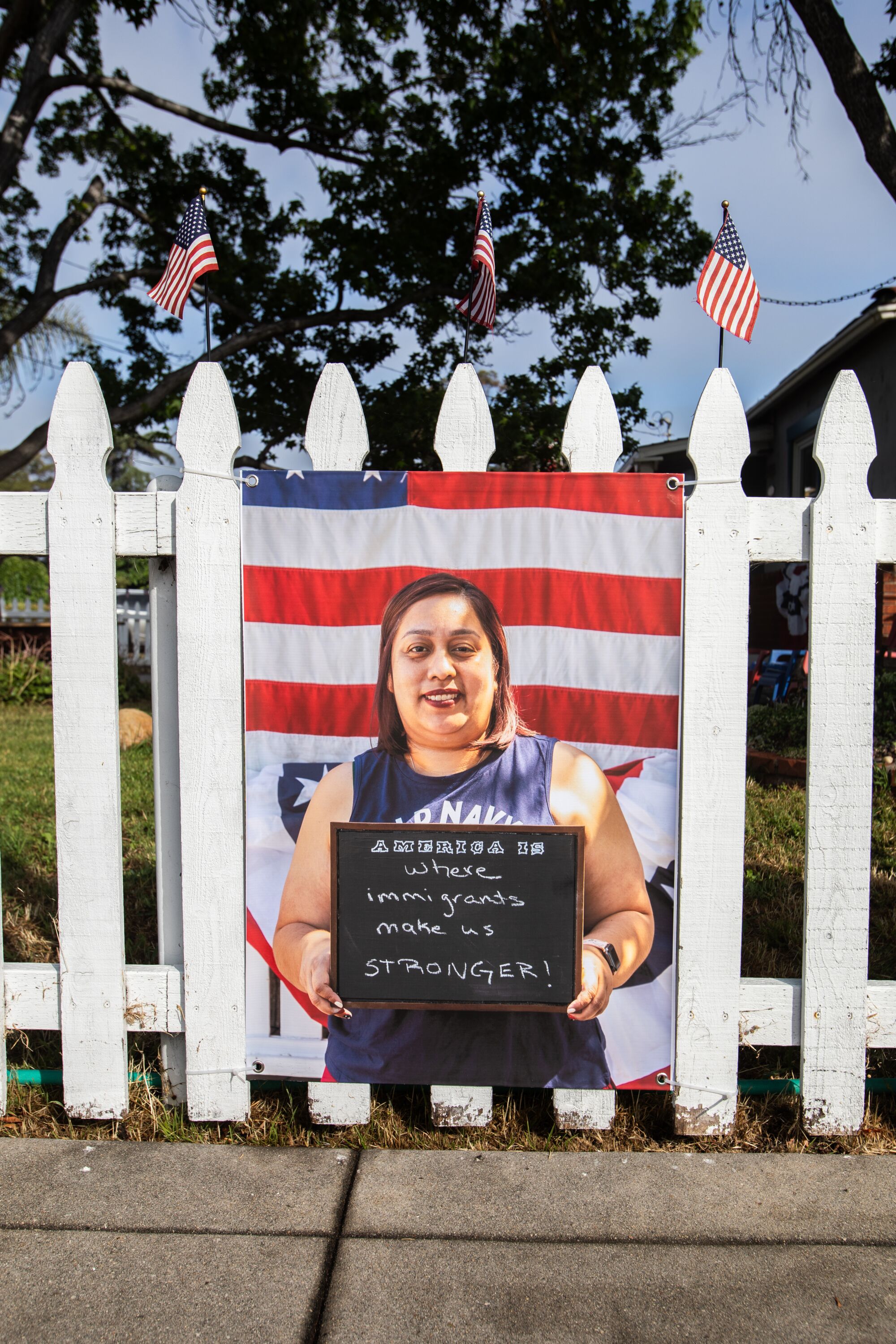   An einem weißen Lattenzaun hängt das Porträt einer Frau mit einem Schild vor einer amerikanischen Flagge 