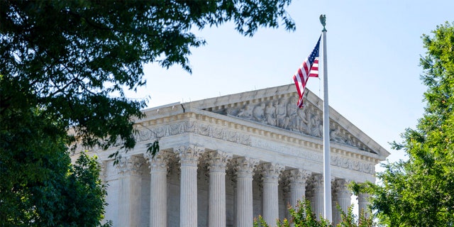 Gebäude des Obersten Gerichtshofs der USA, umrahmt von Bäumen, davor US-Flagge