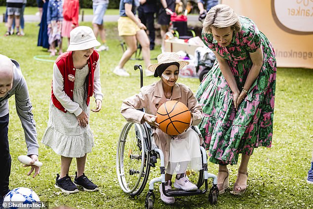 Königin Mathilde lächelt, als sie mit den Kindern spricht, während diese ein sportliches Spiel mit Basketball spielen