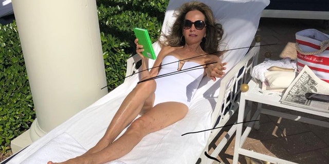 Susan Lucci lounging on a beach chairin a white one-piece 