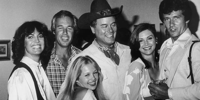 Die Darsteller von Dallas in einer Schwarz-Weiß-Aufnahme lächeln miteinander