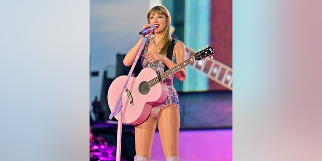 Taylor Swift hält das Mikrofon während der Eras Tour und spielt auf einer rosa Gitarre