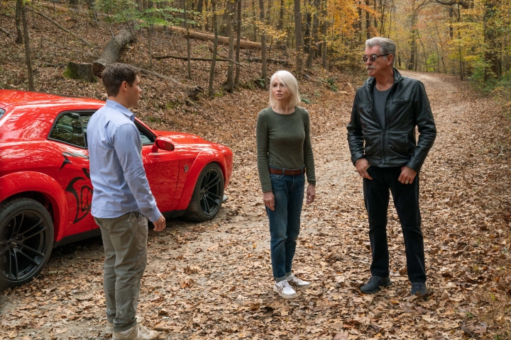 Adam Devine, Ellen Barkin und Pierce Brosnan stehen in The Out-Laws neben einem roten Muscle-Car.